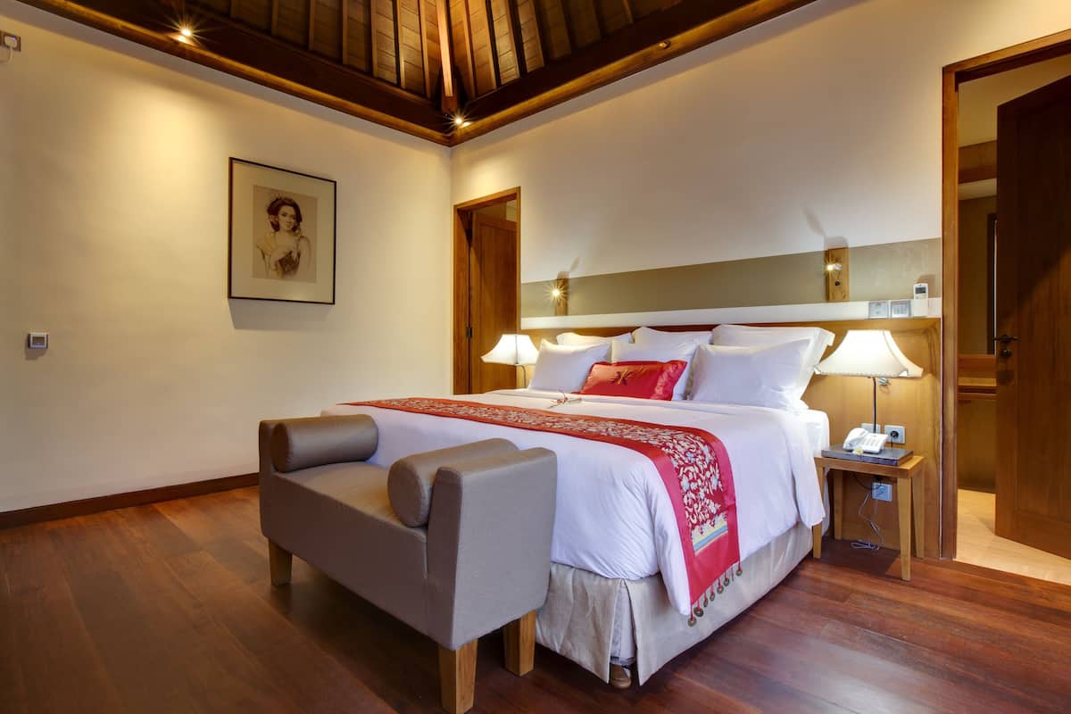 A hotel room with a large bed, bedside lamps, a wooden bench, a framed picture on the wall, and a wooden ceiling.
