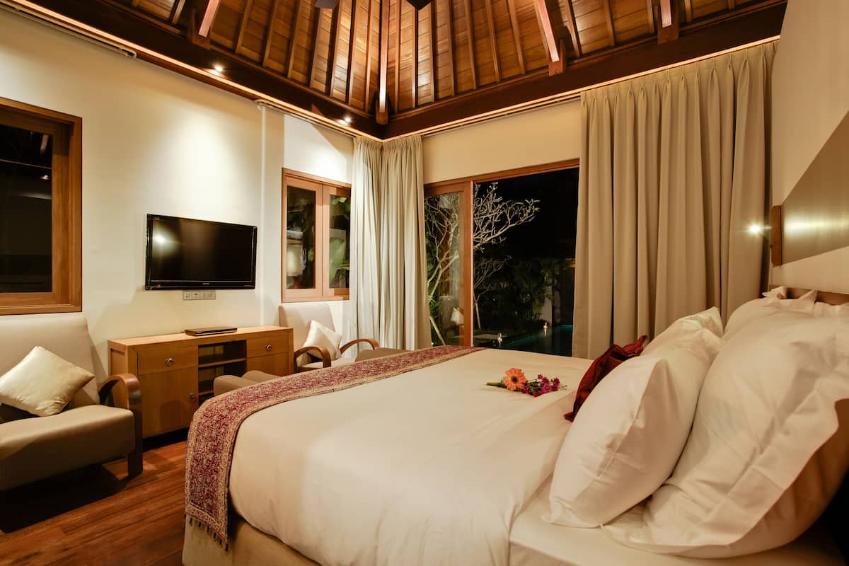 A well-lit bedroom with a large bed, a desk, a television, and a view of the outdoors.