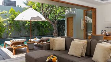 A modern living room with a sofa, a dining table, and a poolside area with lounge chairs and an umbrella.