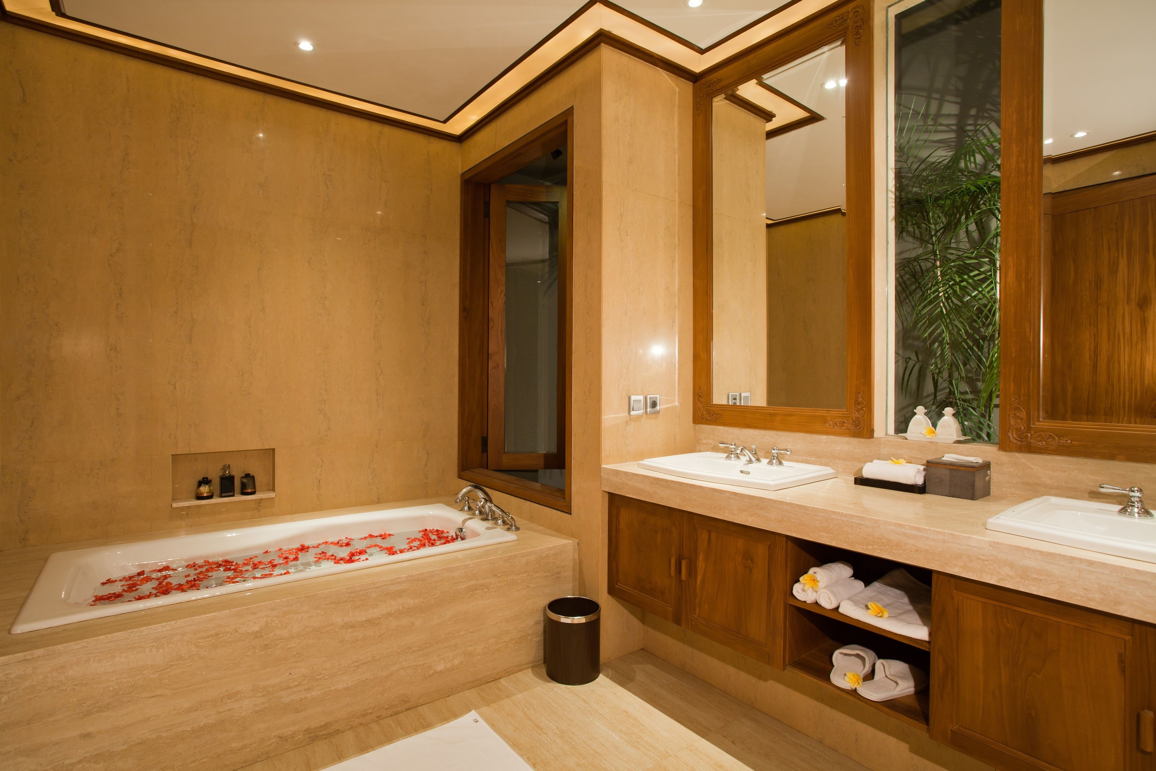 A modern bathroom with a large bathtub, two sinks, wooden cabinetry, and a mirror.