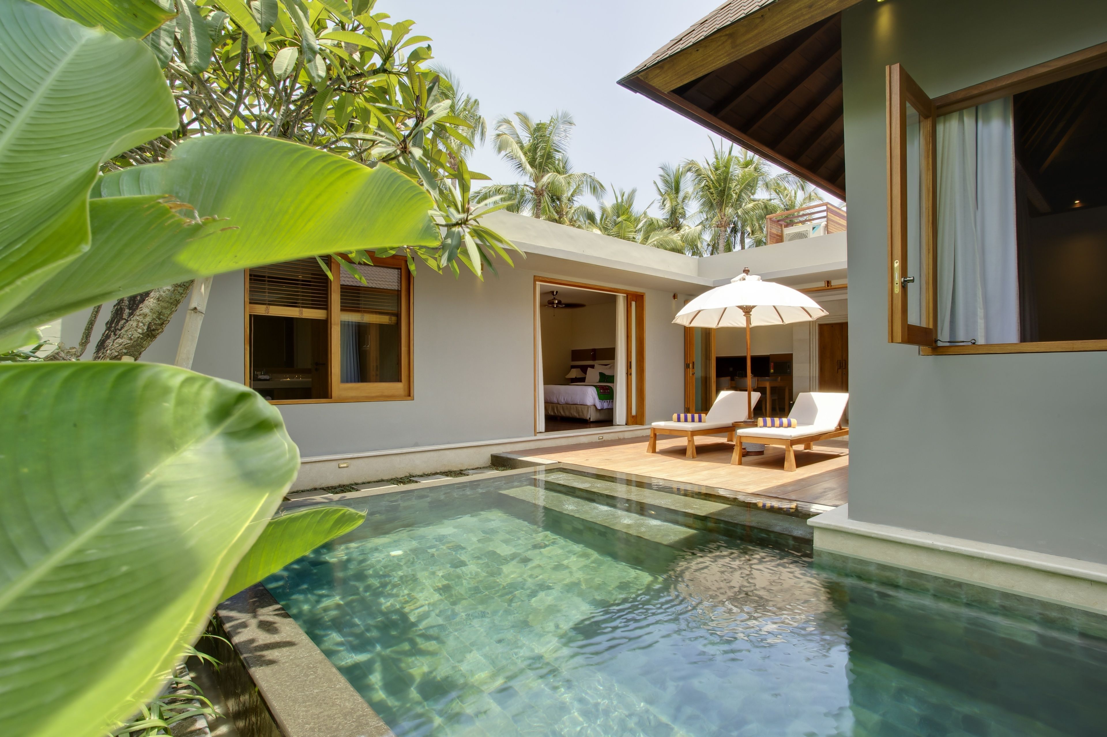 A pool area with clear water, surrounded by tropical plants and a building with a balcony.