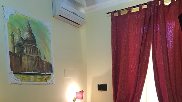 Une chambre d’hôtel avec un grand lit, des rideaux rouges, un tableau au mur et un appareil de climatisation.
