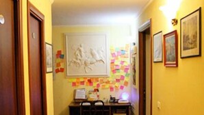 Un couloir avec un banc en bois, un bureau avec un ordinateur et un mur décoré de notes et de photos.
