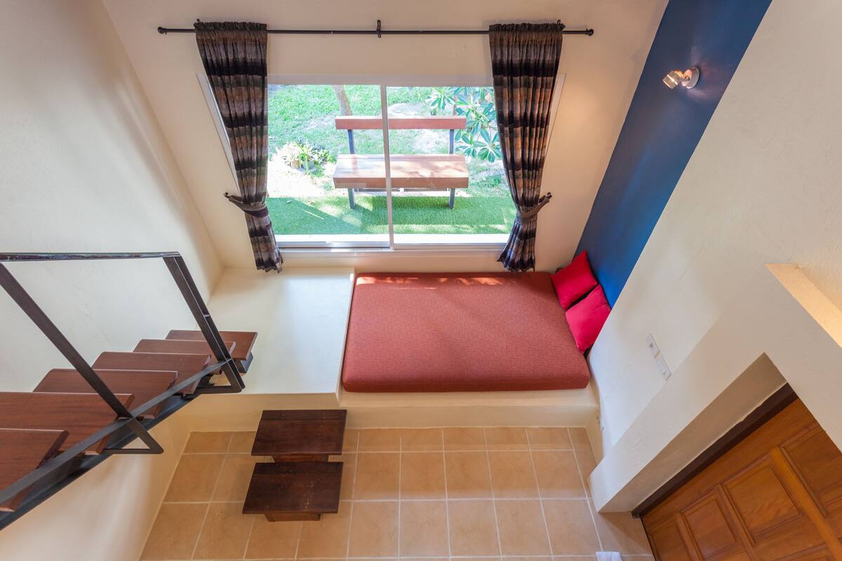 Ein Zimmer mit einem roten Sofa, einer Holzbank vor einem Fenster und einer Treppe.
