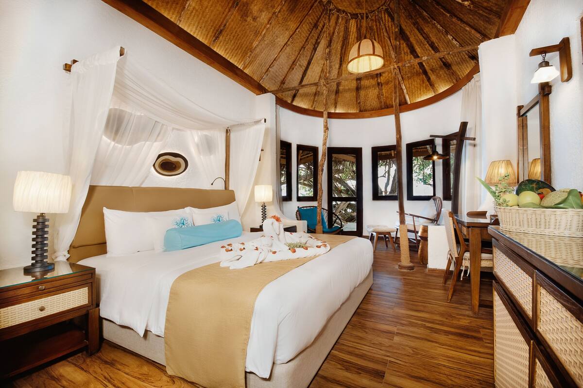 A spacious bedroom with a large bed, a wooden ceiling, and a view of the outdoors.