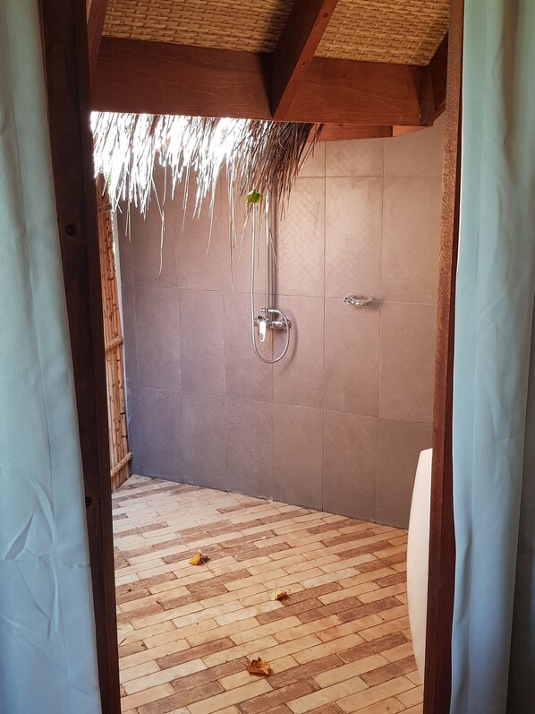 A shower area with a tiled wall, a showerhead, and a wooden ceiling.