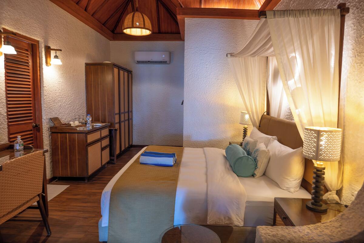 A bedroom with a bed, bedside table, lamp, and a small desk with a chair.