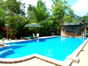 Una piscina al aire libre, sombrillas, sillones reclinables de piscina