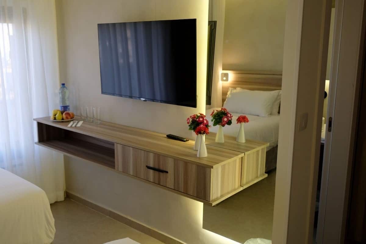 A hotel room with a bed, a bedside table with a remote control, a TV mounted on the wall, and a mirror above the bed.