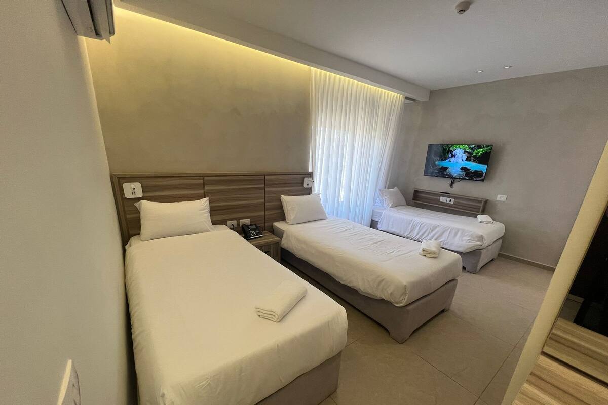 A hotel room with two beds, a TV, and a bedside table.