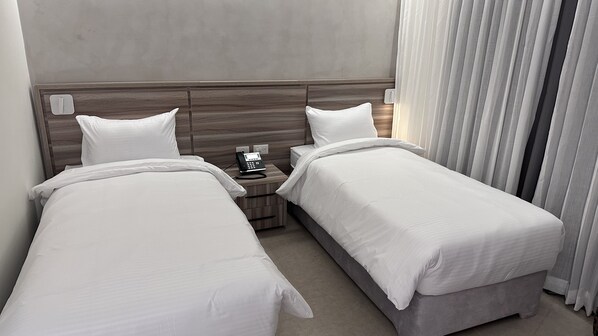 A hotel room with two single beds, a bedside table with a phone, and a window with curtains. - Jerusalem Metropole Hotel (Jerusalem)