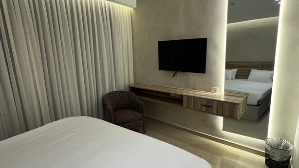 A modern hotel room with a large bed, a TV mounted on the wall, a bedside table, and a mirror reflecting the bed and a nightstand. - Jerusalem Metropole Hotel (Jerusalem)