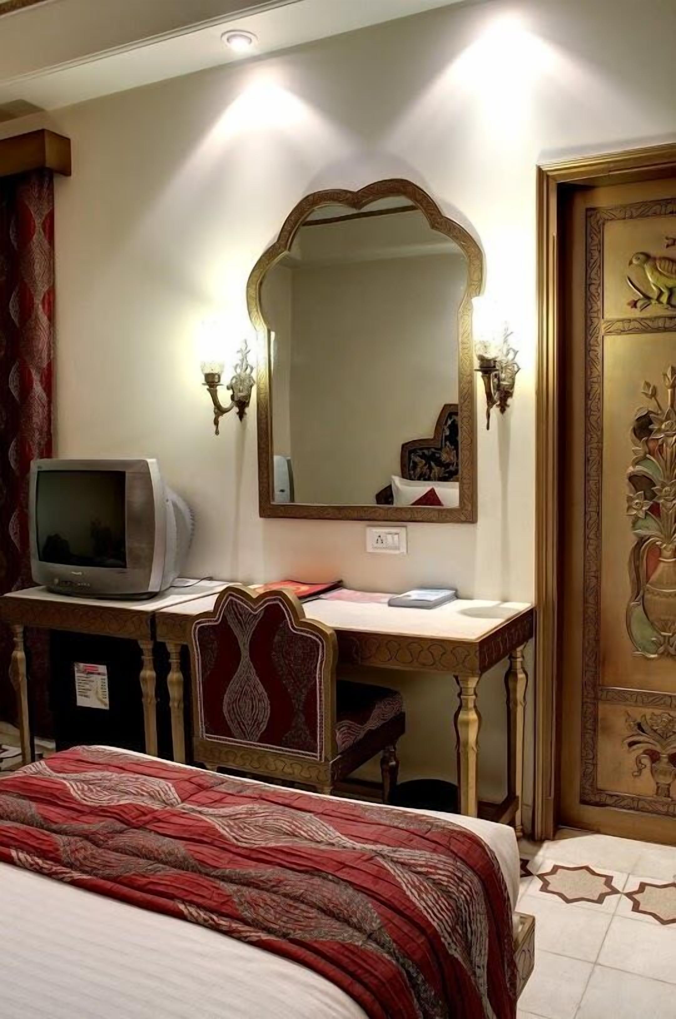 Ein Hotelzimmer mit einem Bett, einem Schreibtisch mit Fernseher, einem Spiegel und einer Tür mit dekorativen Paneelen.