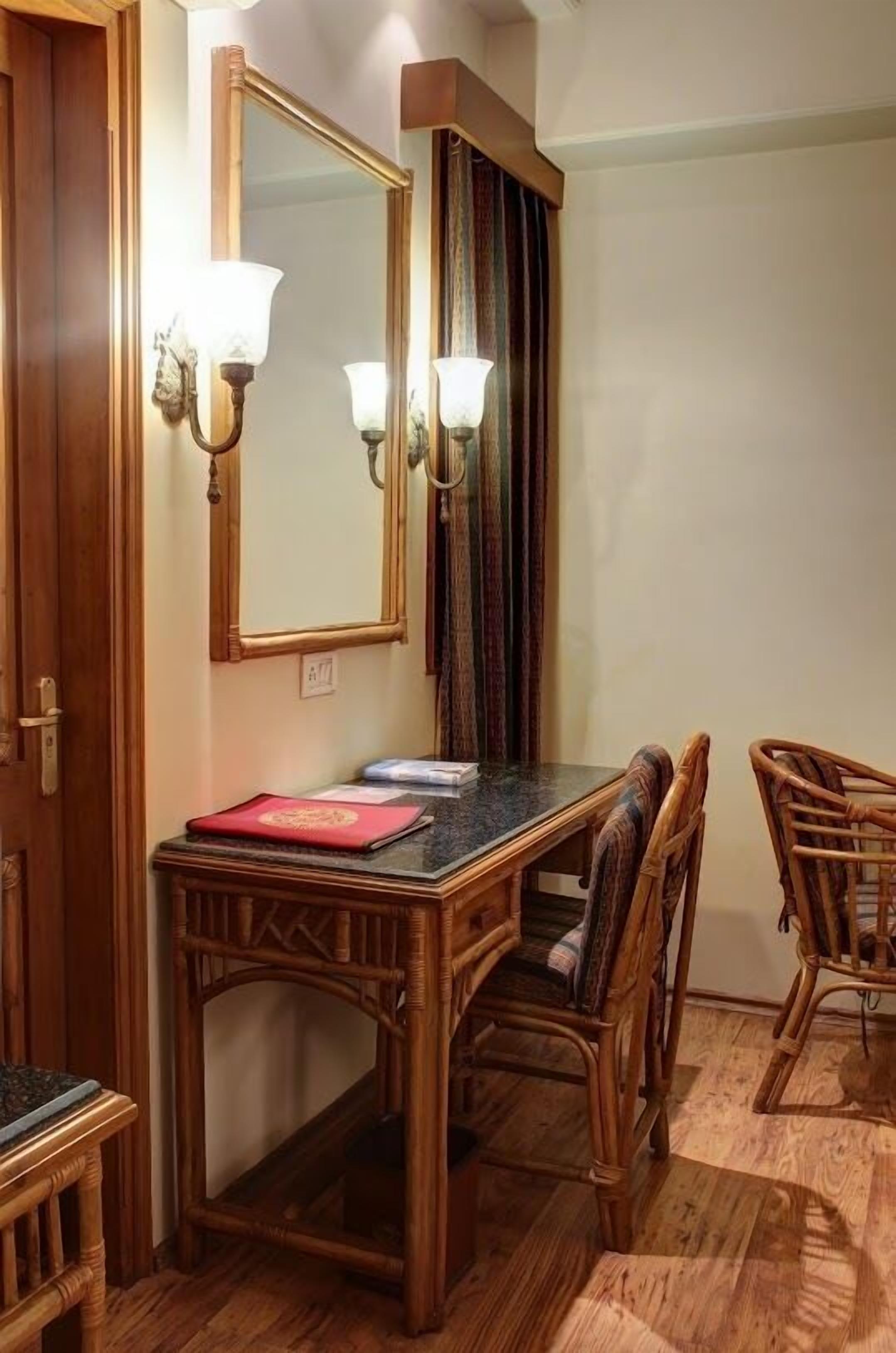 Un comedor con una mesa de madera, cuatro sillas de mimbre, dos lámparas fijadas a la pared y un espejo sobre la mesa.