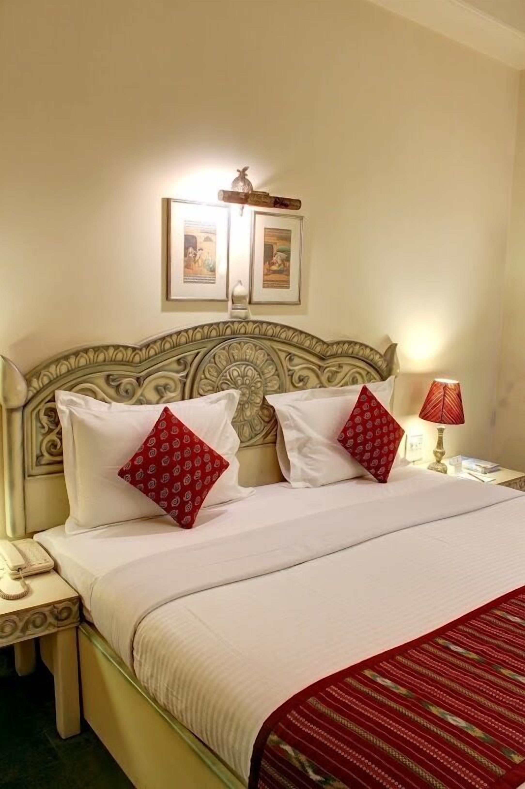 A neatly made bed with a red and white patterned pillow, a bedside lamp, and a framed picture above the bed.