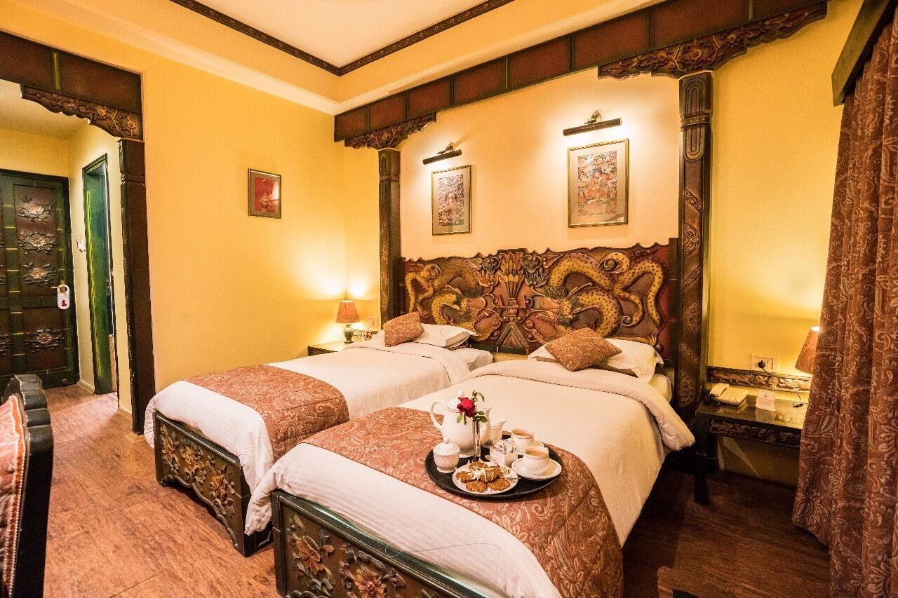 Habitación de hotel con dos camas, cabeceros ornamentados y una bandeja con alimentos para el desayuno sobre la cama.