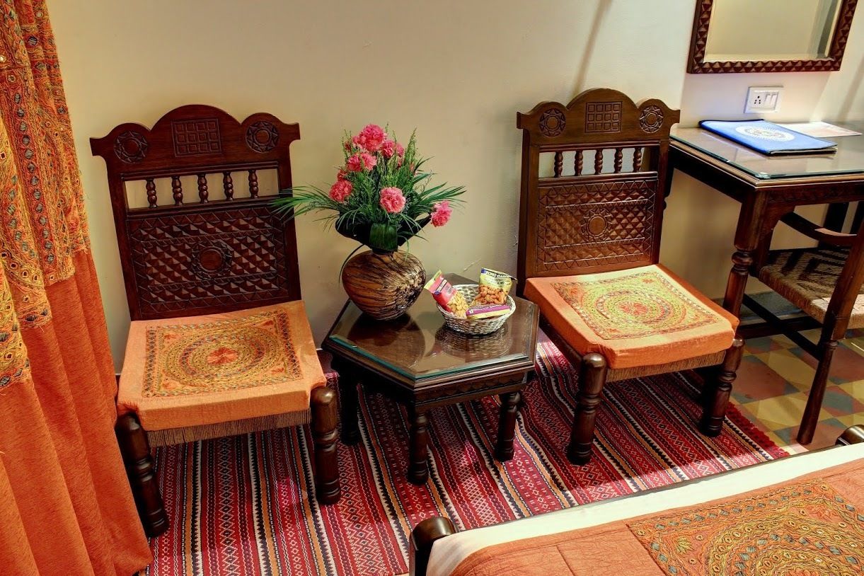 A room with two wooden chairs with intricate back designs, a small table with a vase of flowers, and a laptop on a desk.