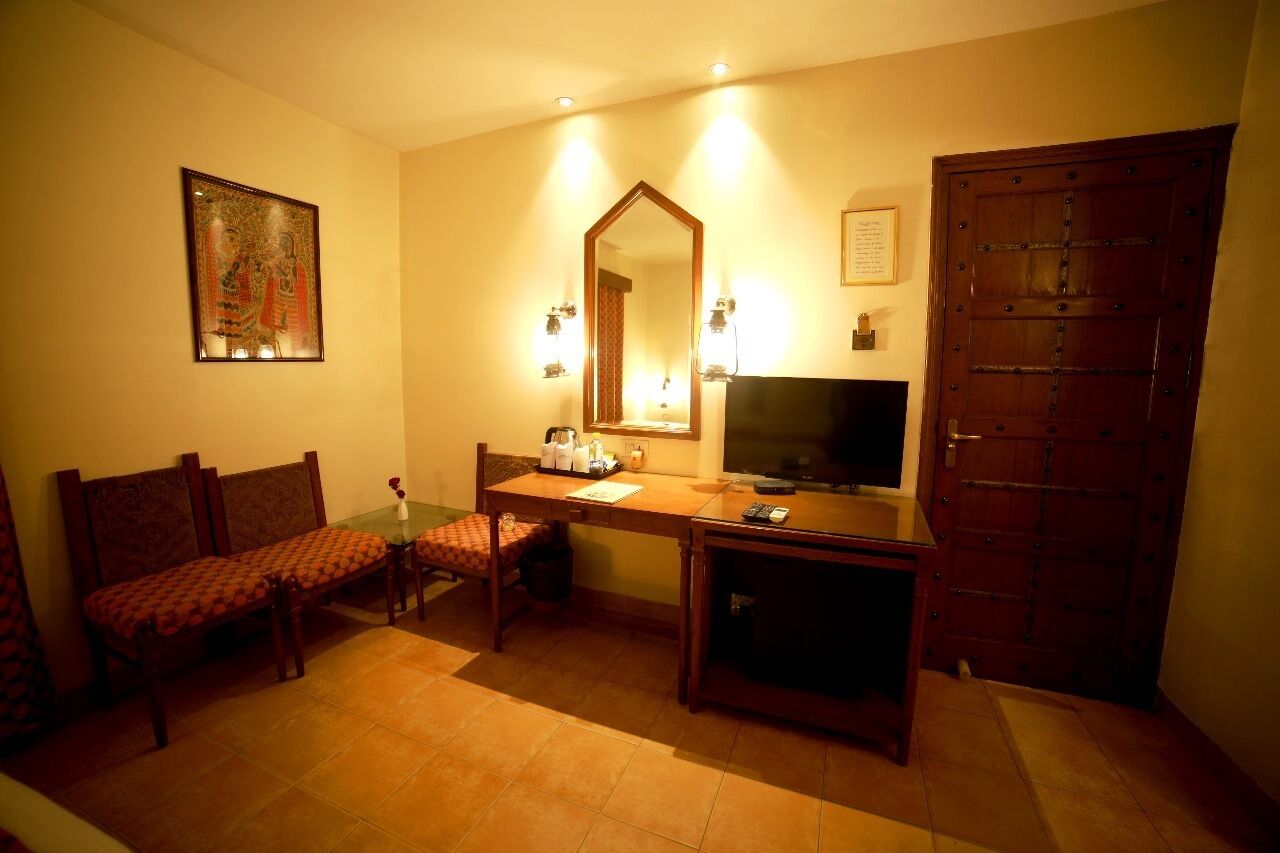 A hotel room with a wooden desk, a television, a large mirror, a sofa, and a door.