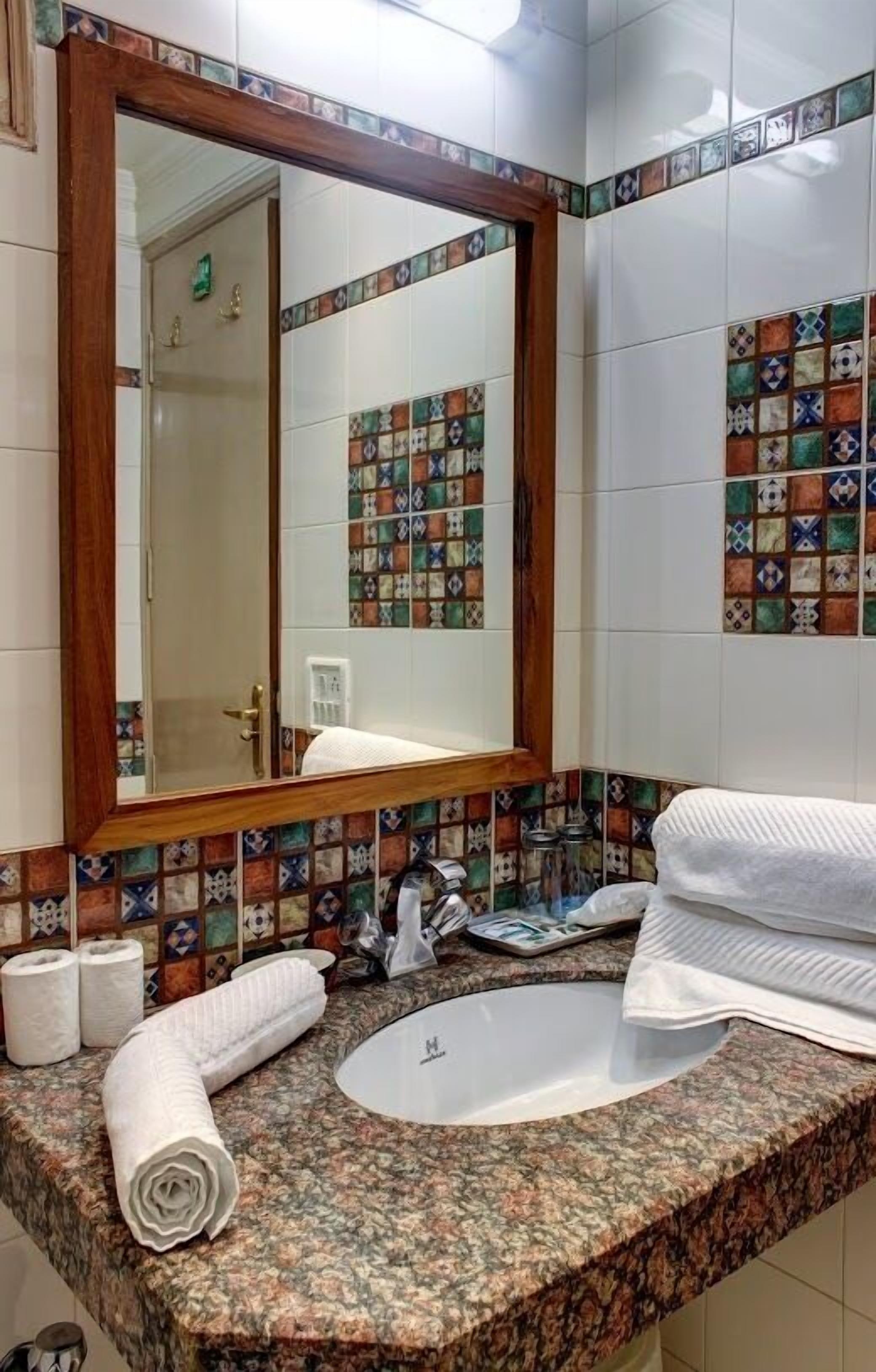 Ein Badezimmer mit einem großen Spiegel, einem Waschbecken und einer Fliesenküchenzeile.