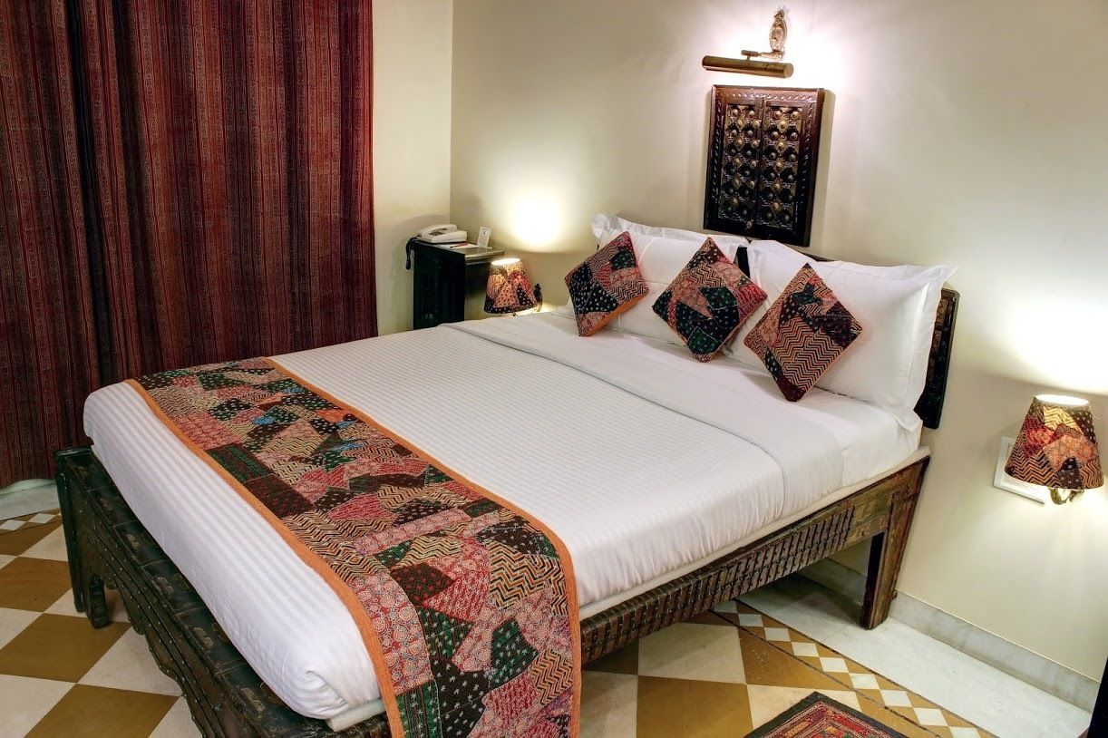 Una cama bien hecha con una colcha estampada y almohadas, una mesita de noche con una lámpara y un panel decorativo en la pared.