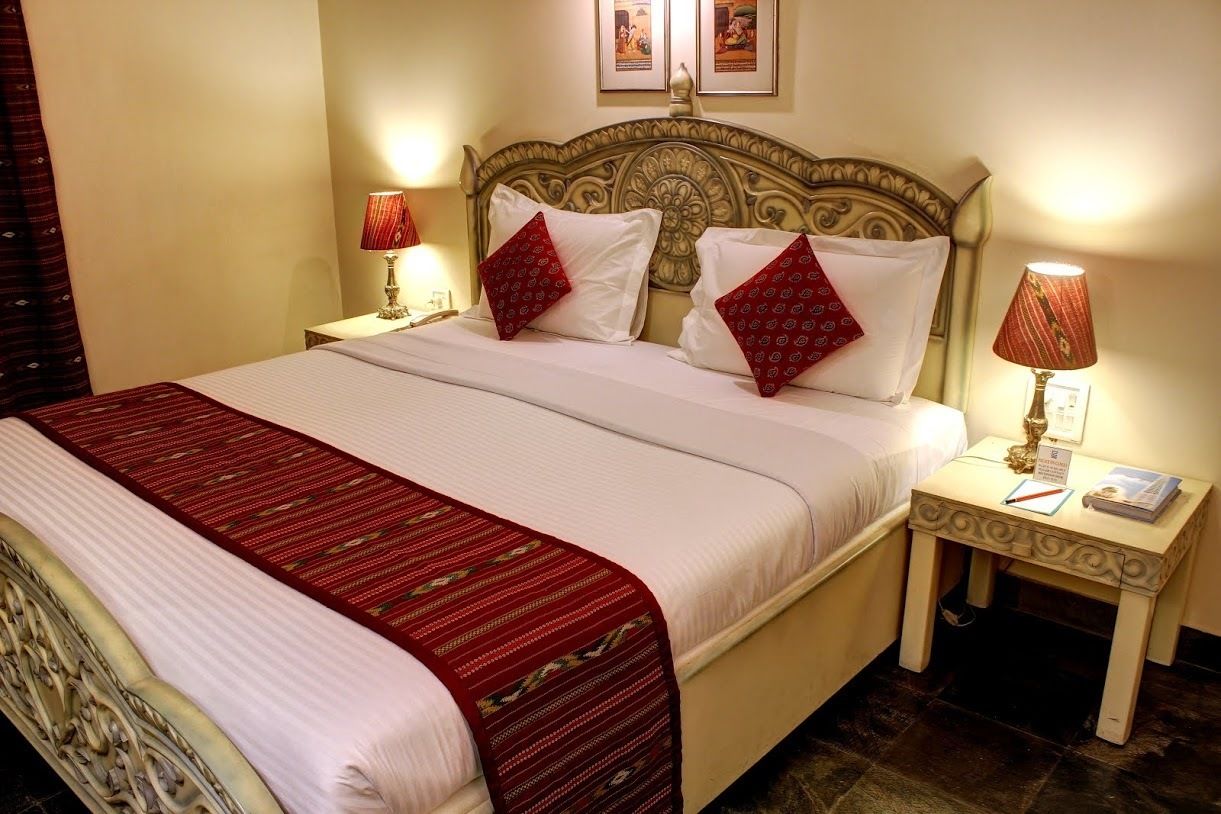 Una habitación de hotel con una cama grande, dos lámparas de noche, una mesita de noche y un cabecero con intrincados grabados.