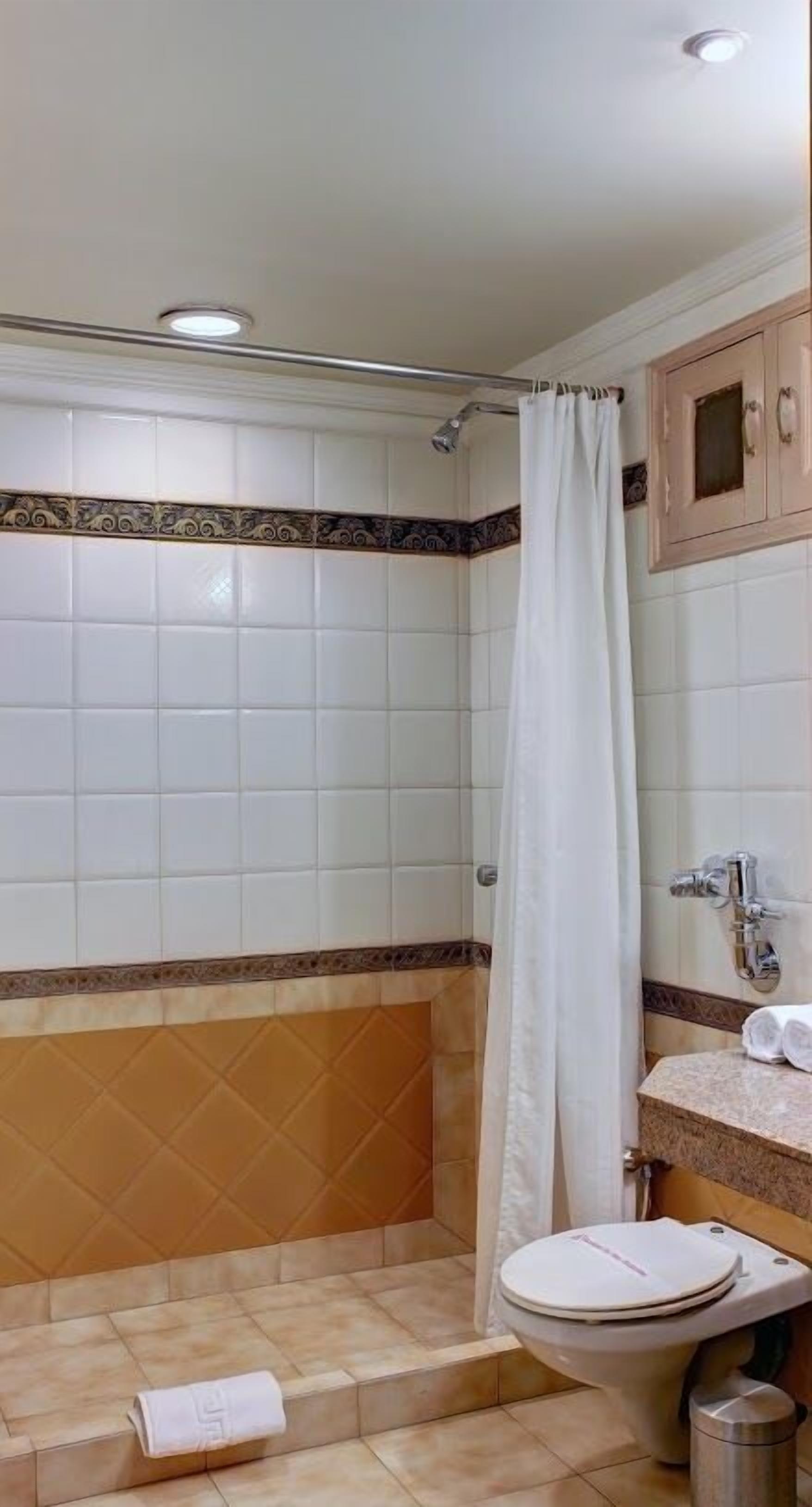 A bathroom with white tiles, a shower curtain, a sink, and a toilet.