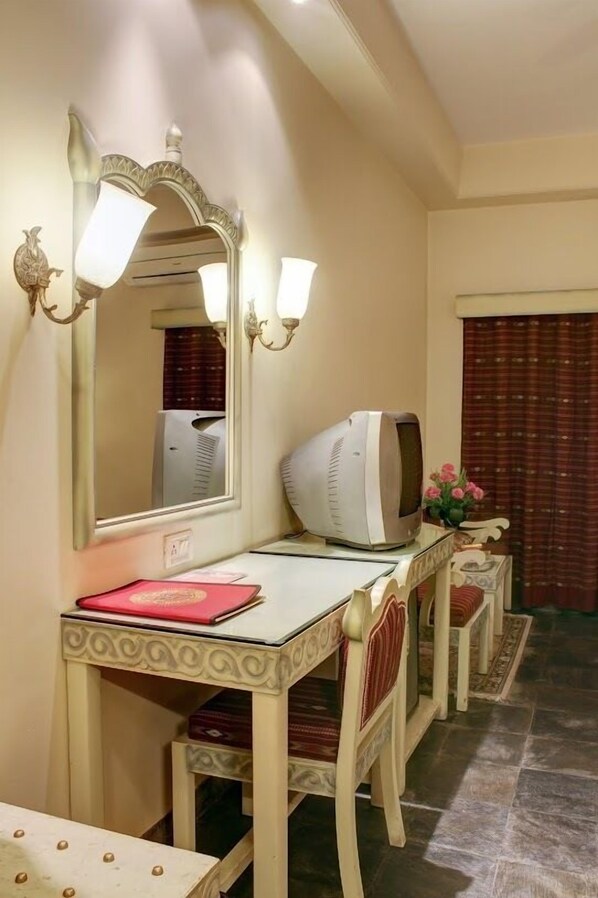 A hotel room with a vanity area featuring a mirror, a television, and a small table with a red book.