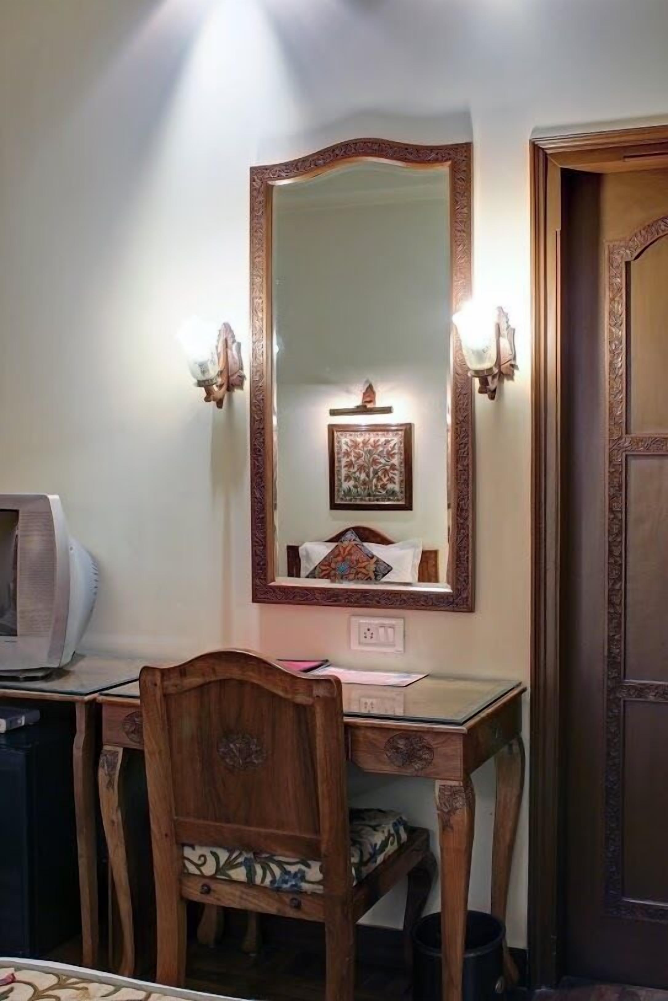 Une pièce comprenant un bureau en bois, une chaise, un grand miroir avec un cadre orné et une porte dotée de panneaux décoratifs.