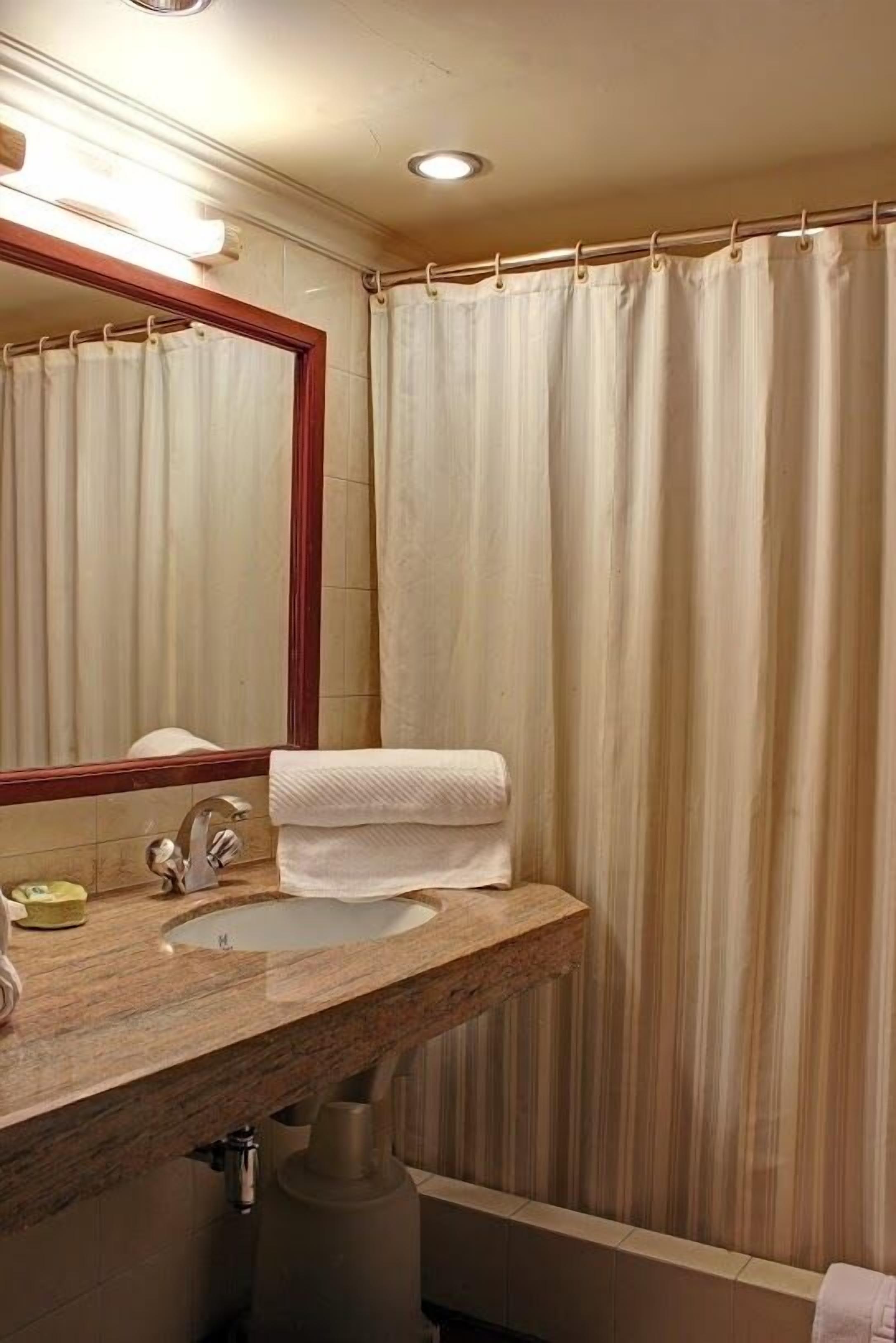 A bathroom with a marble sink, a mirror, and a shower curtain.