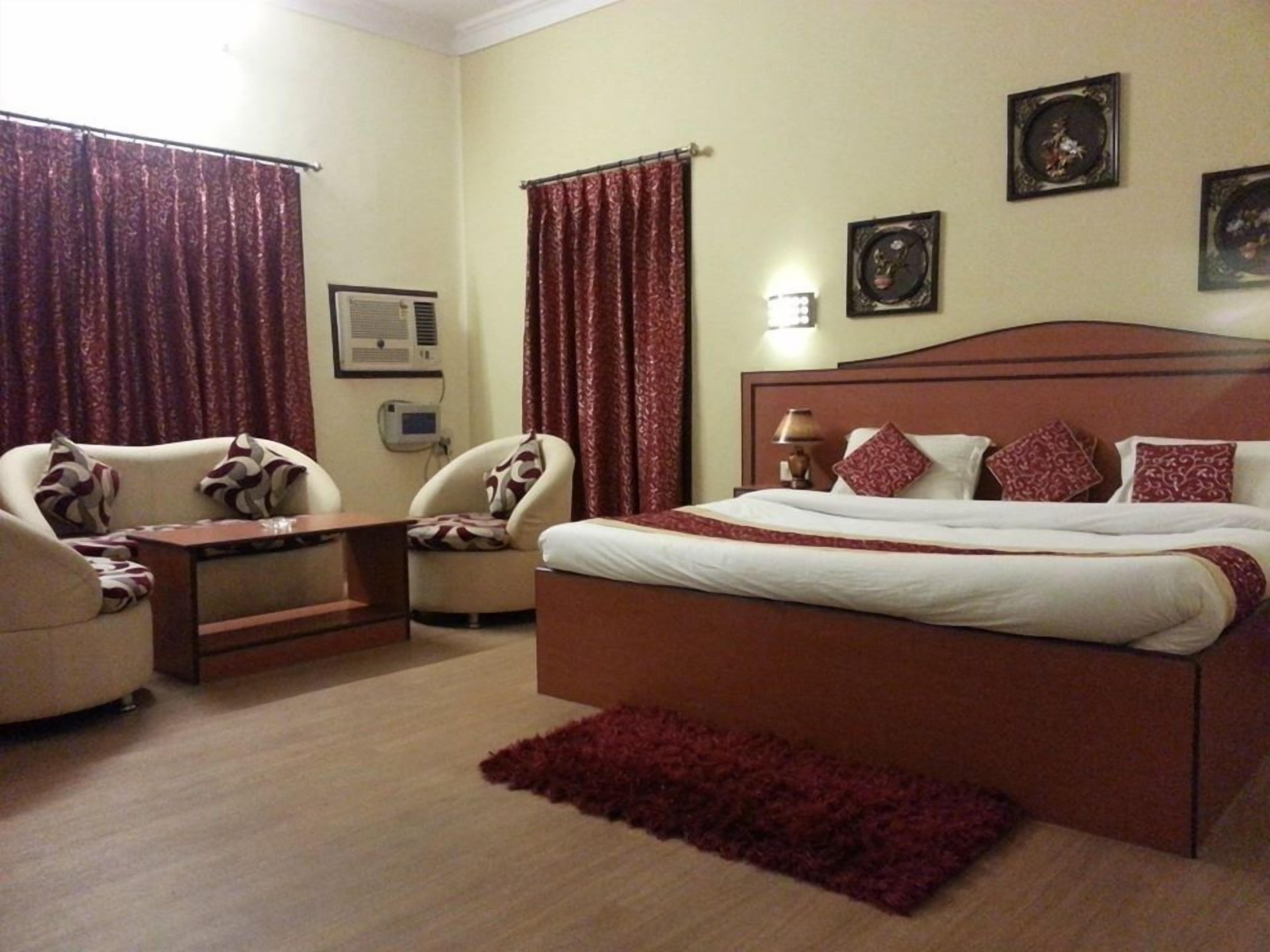A hotel room with a bed, two armchairs, a small table, a red rug, and two curtains.