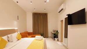 A hotel room with a bed, a sofa, a TV, and a mirror. - Hotel Varuna (Varanasi)