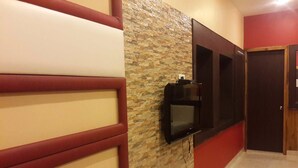 A hallway with a stone wall, a mounted flat-screen TV, and a door. - Hotel Varuna (Varanasi)