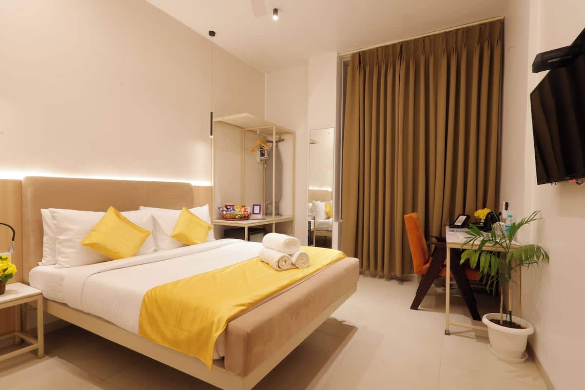 A hotel room with a large bed, a desk, a chair, a potted plant, and a bathroom area.