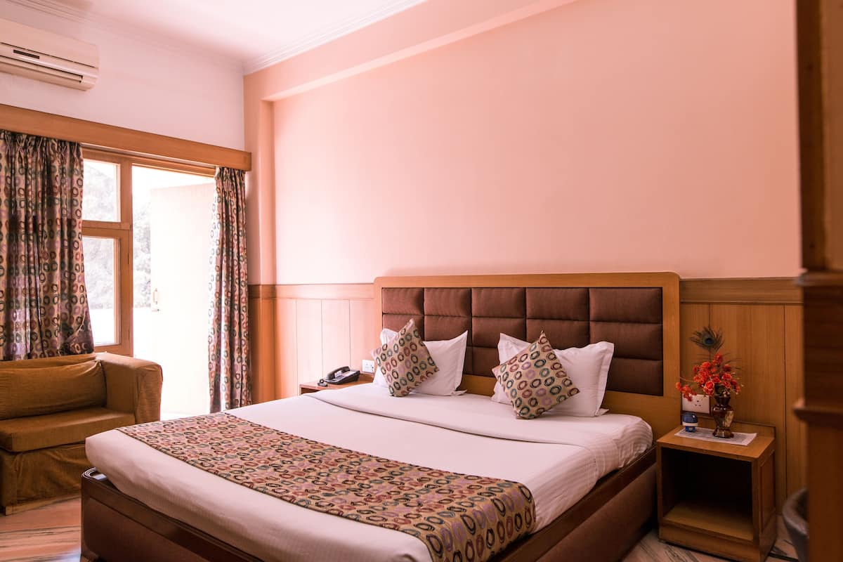 A hotel room with a bed, a nightstand, a chair, and a window with curtains.