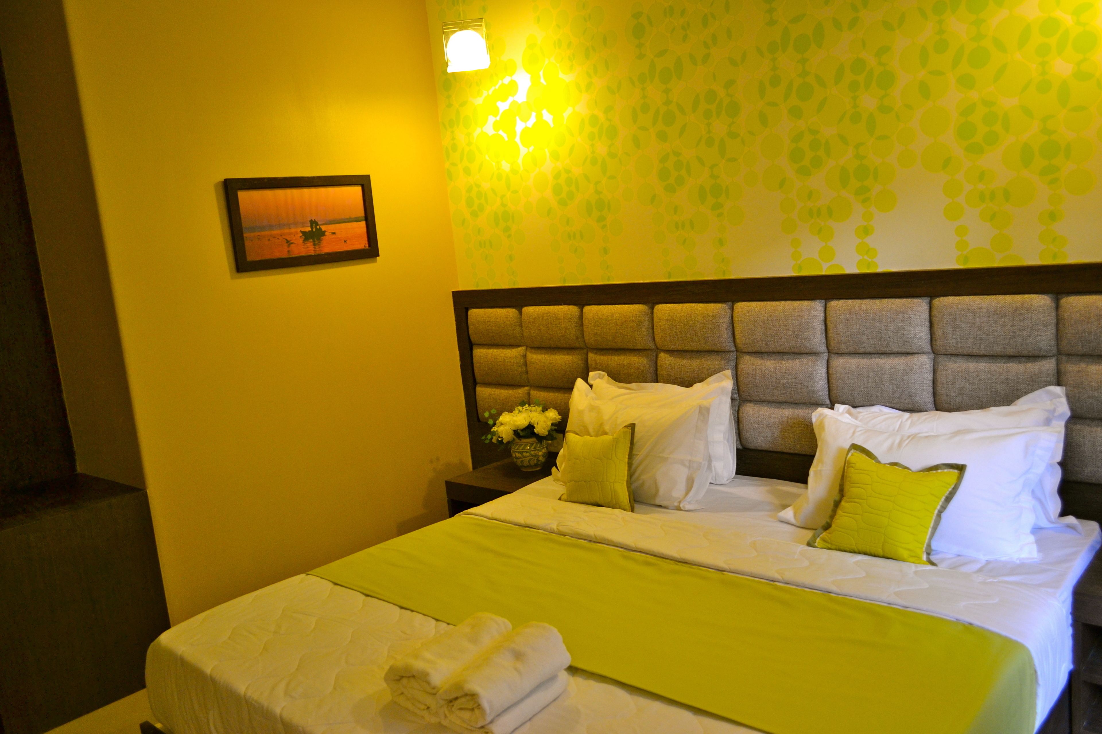 A hotel room with a neatly made bed, a nightstand with a vase of flowers, and a wall with a leaf pattern.