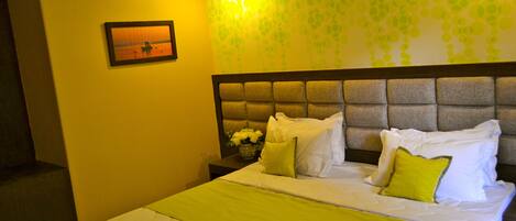 A hotel room with a neatly made bed, a nightstand with a vase of flowers, and a wall with a leaf pattern.