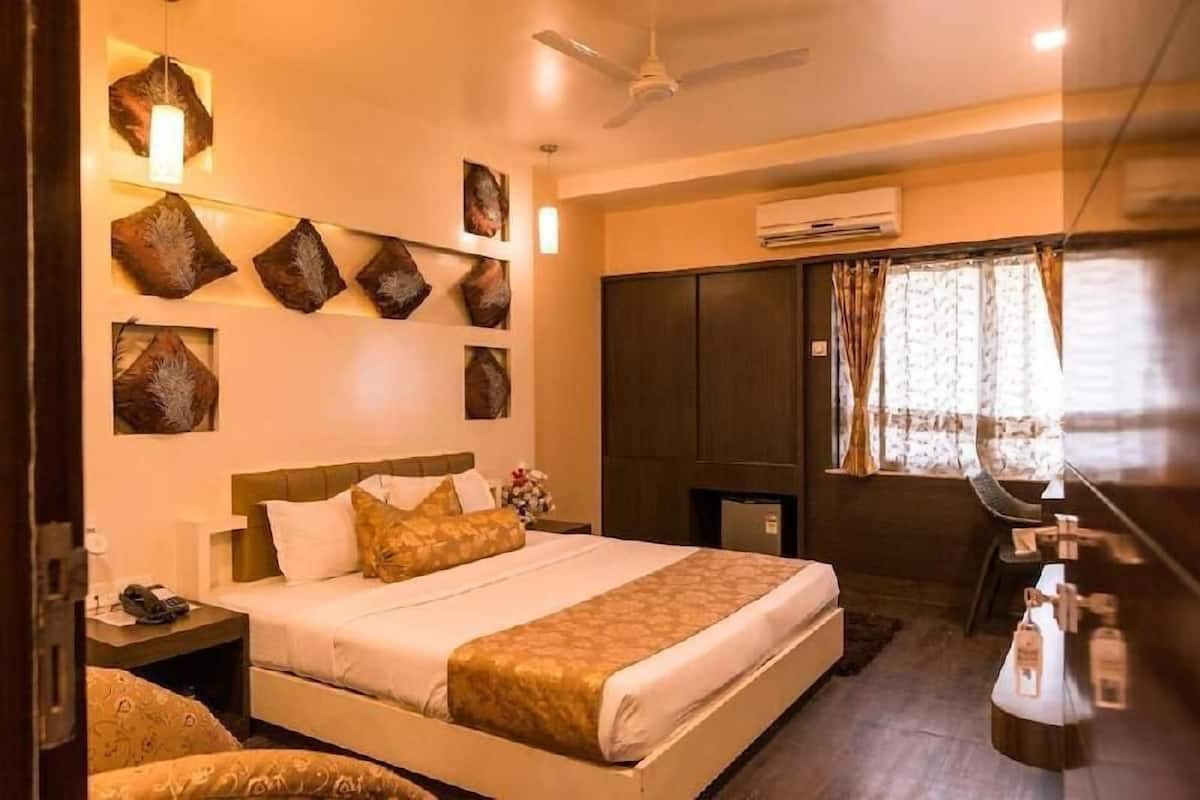 A hotel room with a bed, bedside table, nightstand, wall art, wardrobe, and a window with curtains.