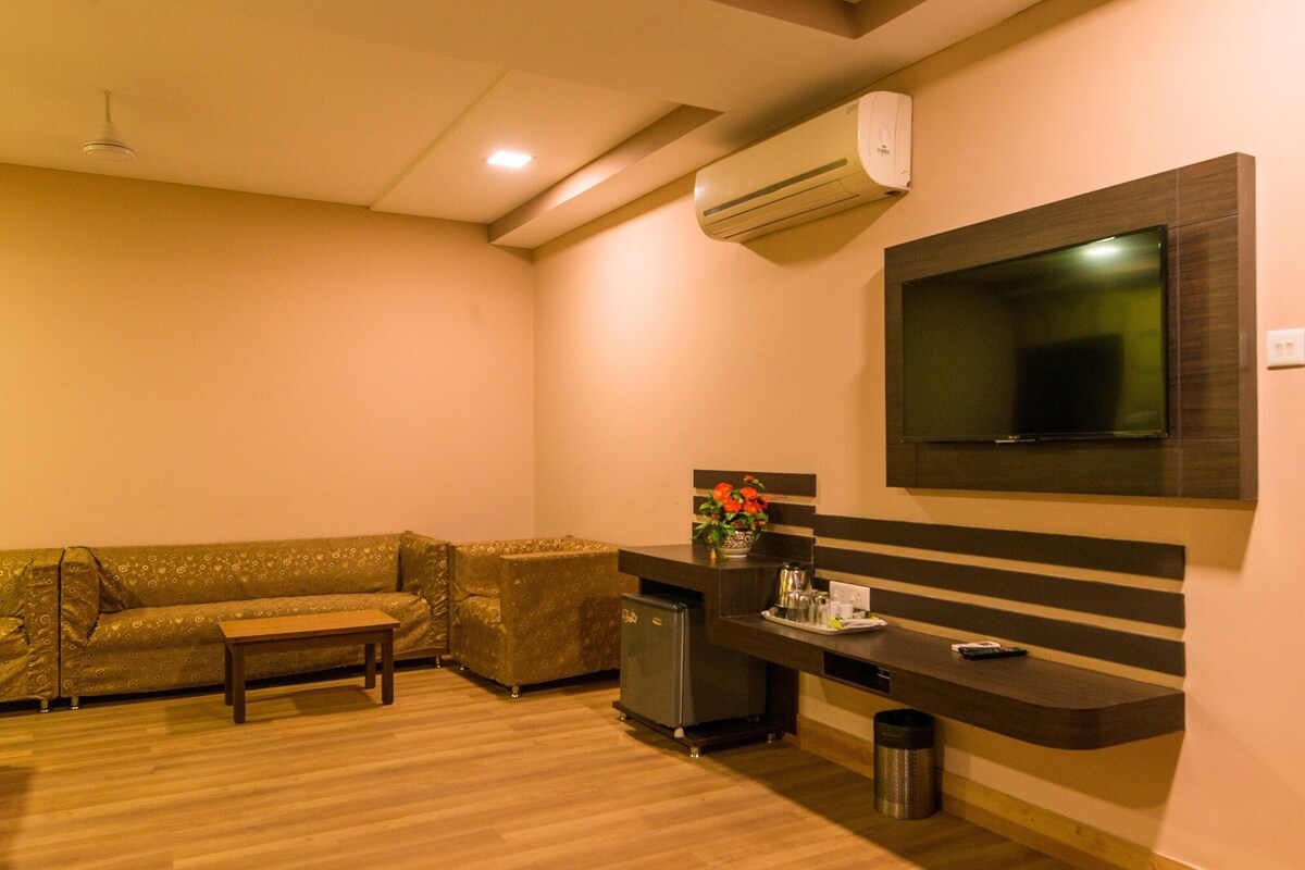 A room with a sofa, a small table, a TV mounted on the wall, and an air conditioning unit.