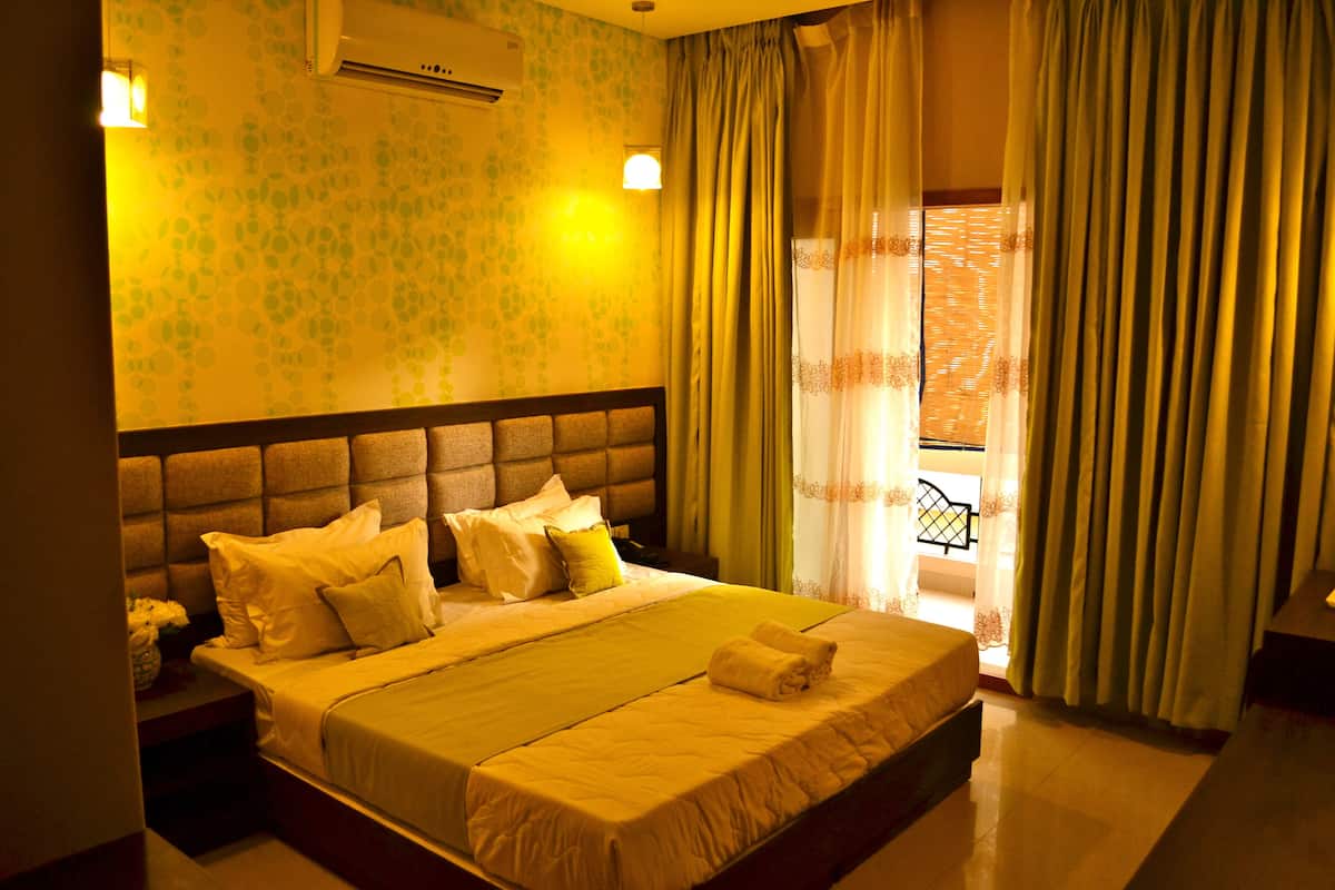 A hotel room with a large bed, a headboard, a nightstand, and a window with curtains.