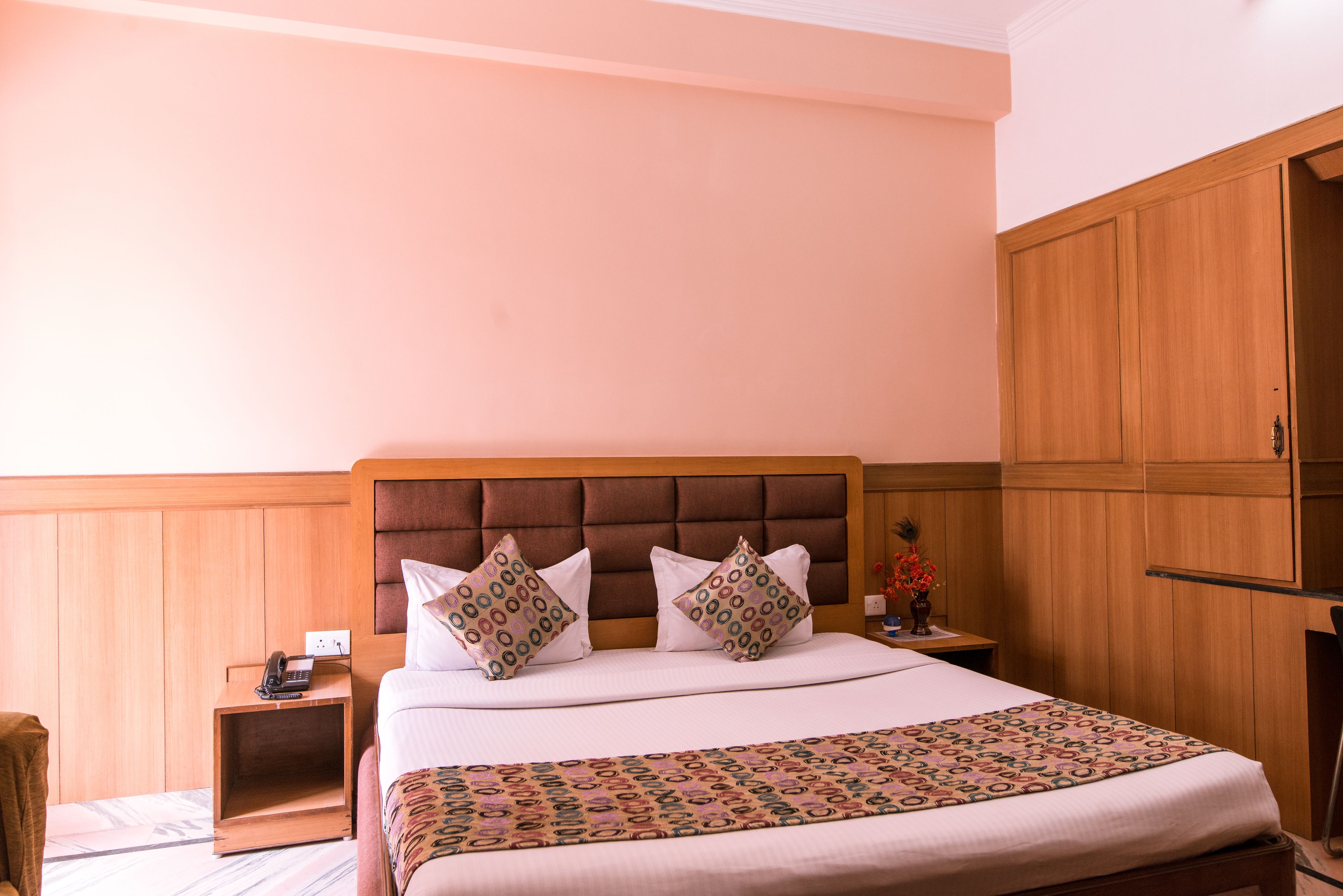 Quarto de hotel com uma cama grande, cabeceira de madeira e mesa de cabeceira com telefone.