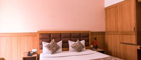 Quarto de hotel com uma cama grande, cabeceira de madeira e mesa de cabeceira com telefone.