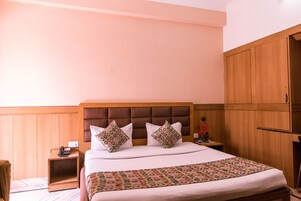 Una camera d'albergo con un letto grande, una testiera in legno e un comodino con un telefono.