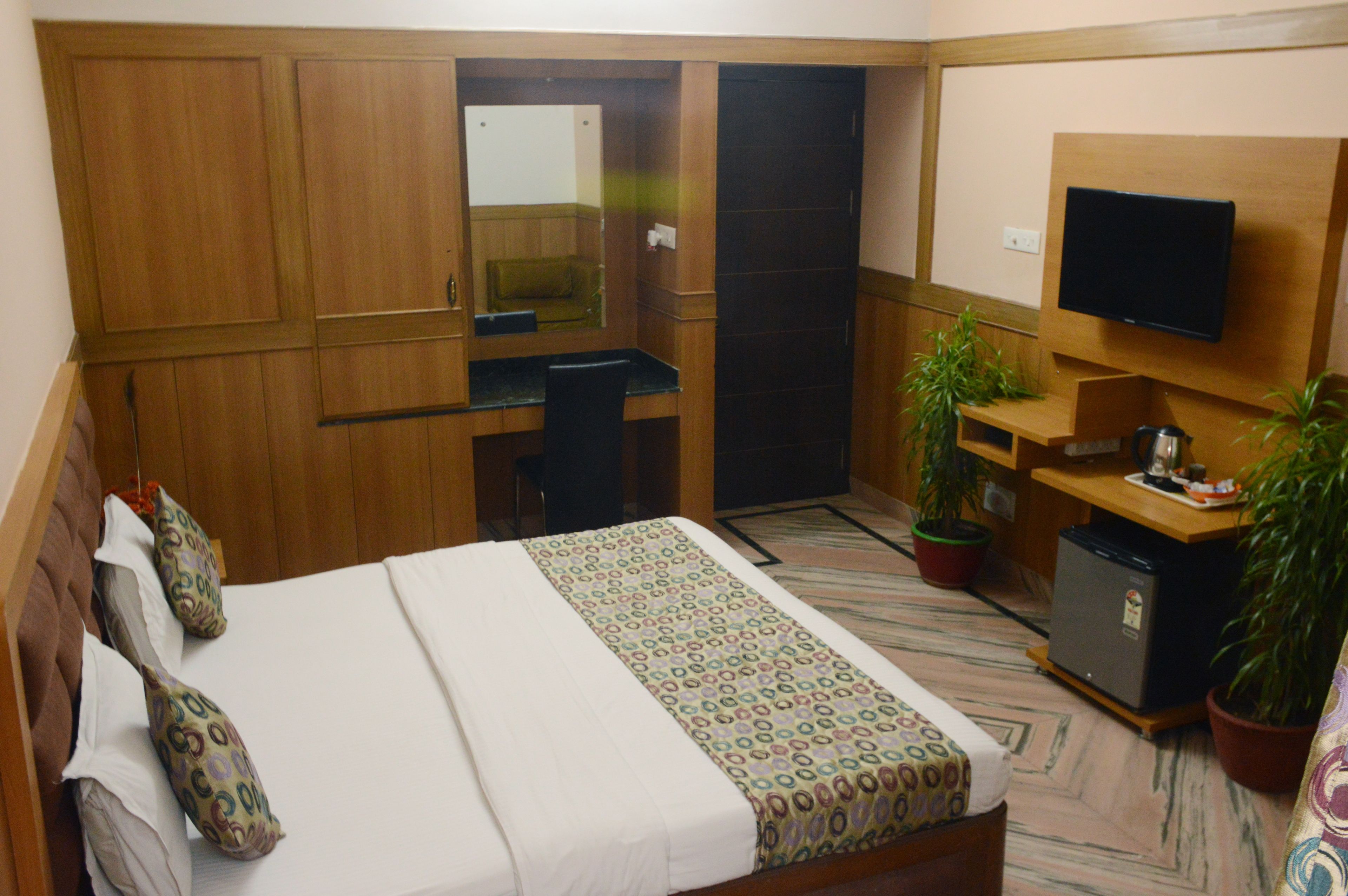 Une chambre d’hôtel avec un lit, un bureau, une télévision et des plantes en pot.