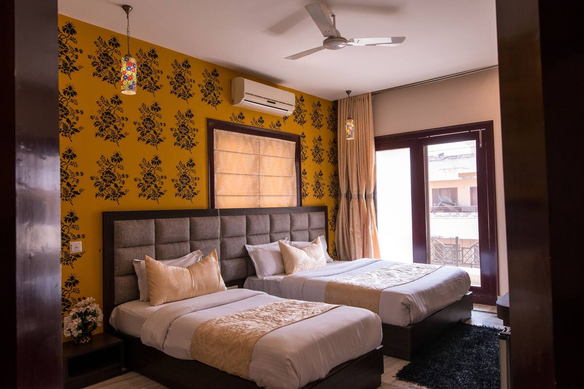 A hotel room with two beds, a ceiling fan, an air conditioning unit, and a view of the outside through a glass door.