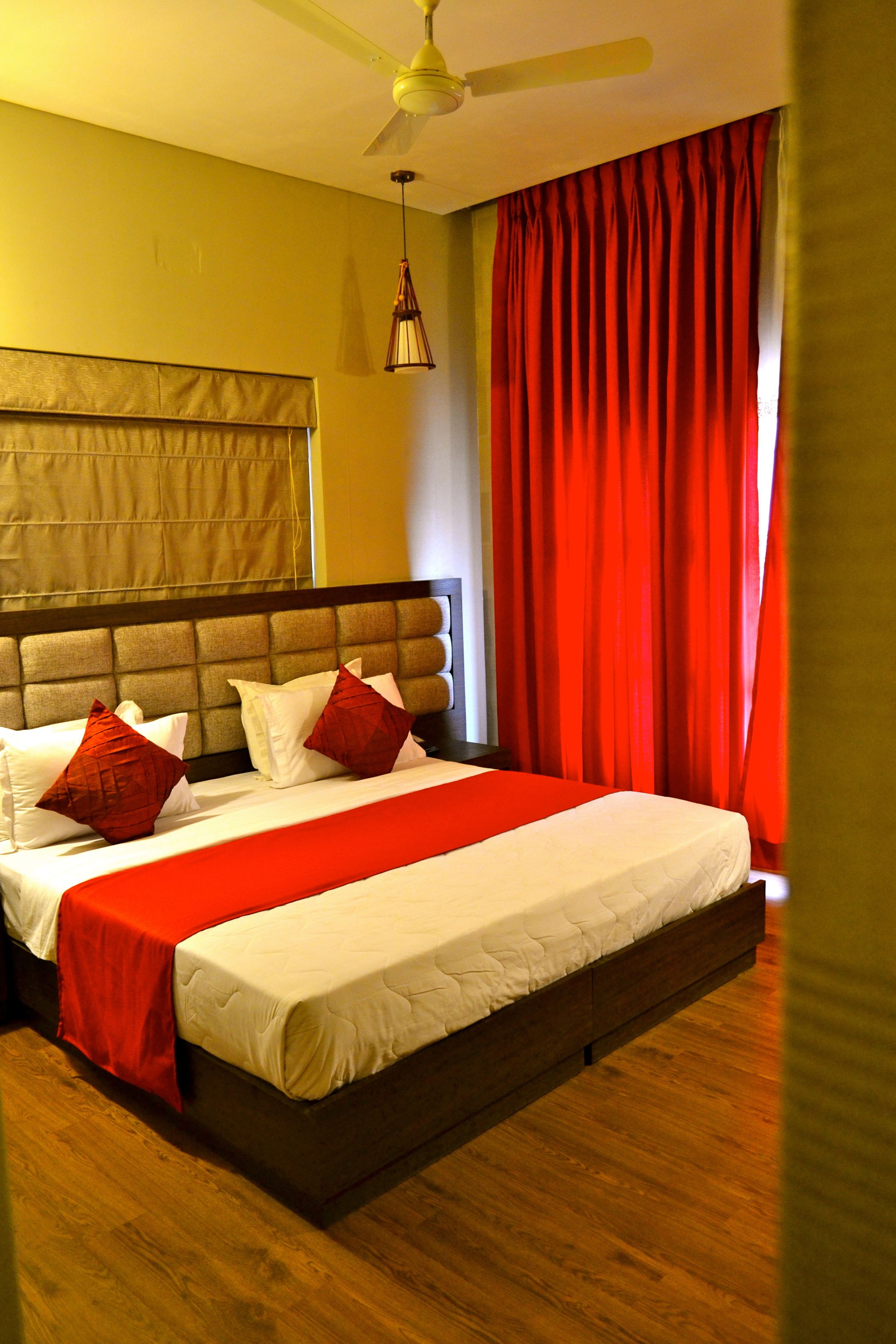 Ein Hotelzimmer mit einem großen Bett, einem Deckenventilator und roten Vorhängen.