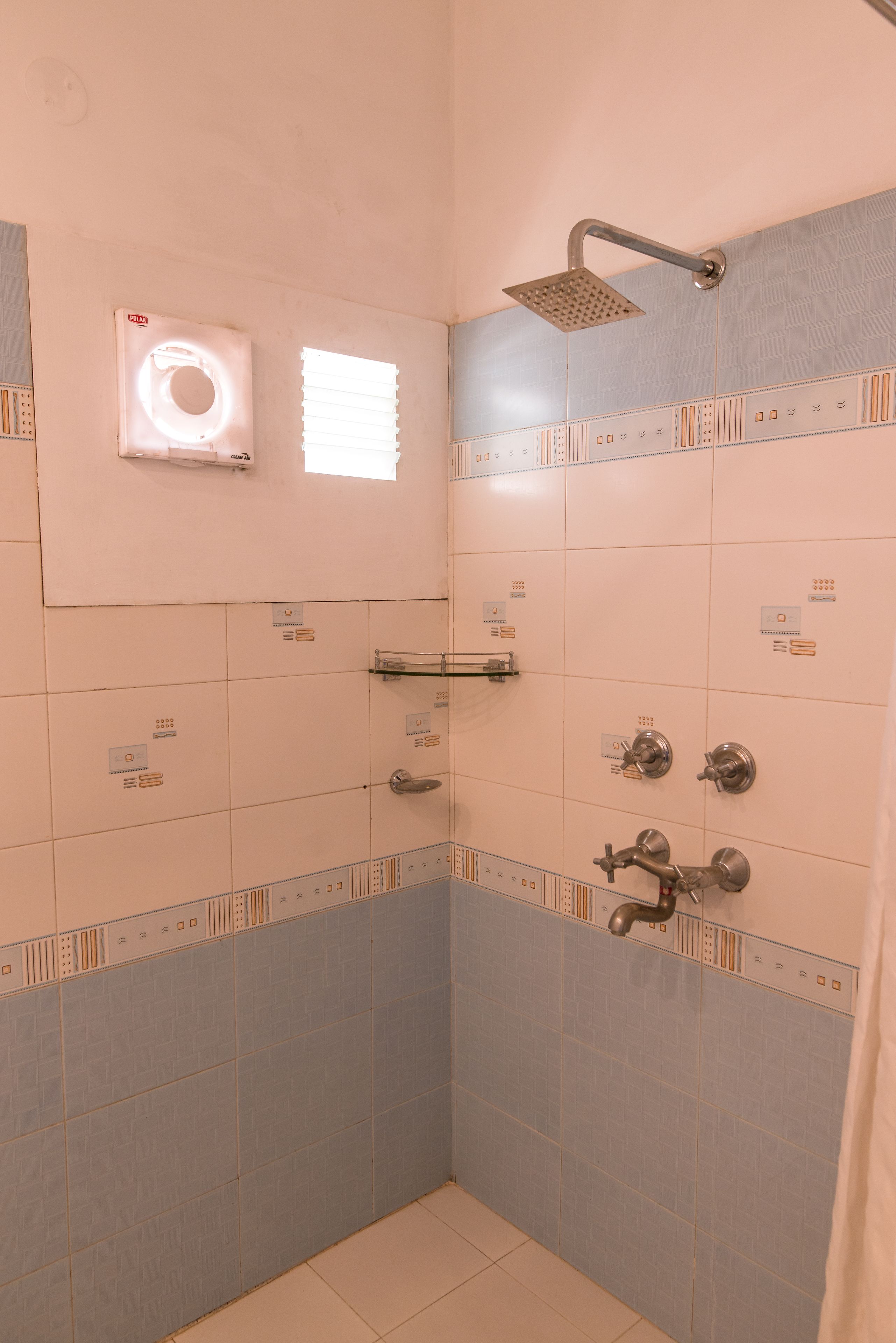 A small, tiled shower area with a handheld showerhead, a towel rack, and a window with blinds.