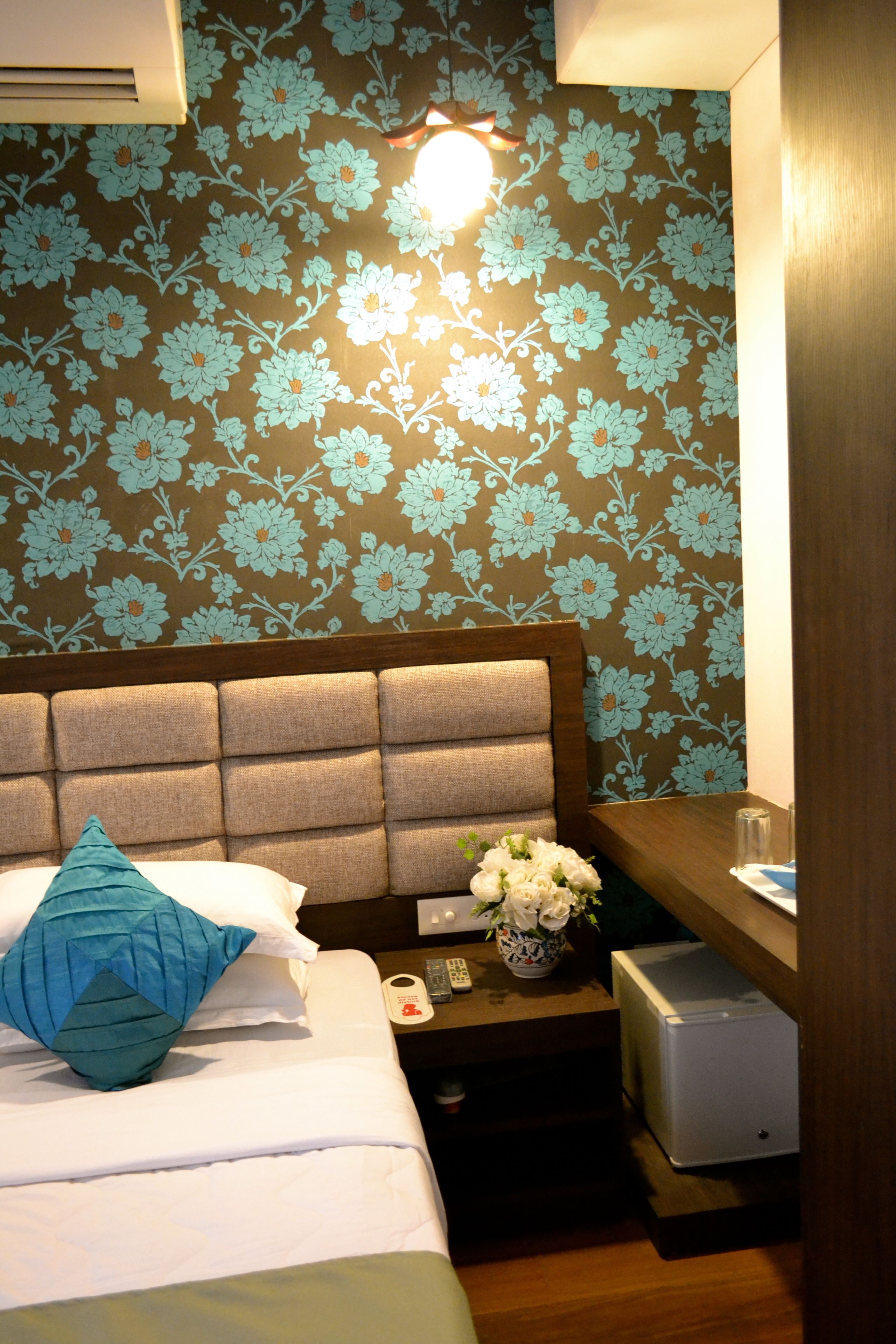Habitació d'hotel amb un llit, una taula de nit, un vas amb flors i una taula petita amb un comandament a distància.