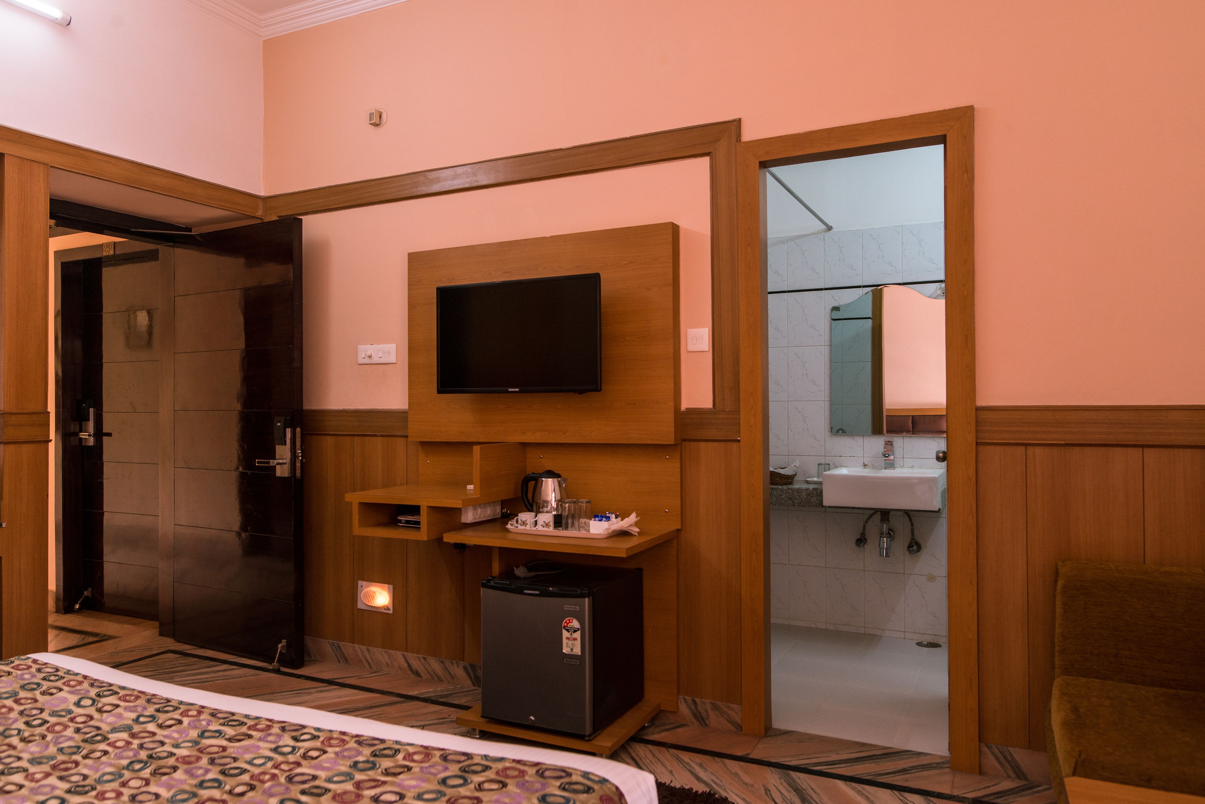 Quarto de hotel com uma cama, televisão fixada na parede, um pequeno frigorífico e uma casa de banho visível através de uma porta aberta.