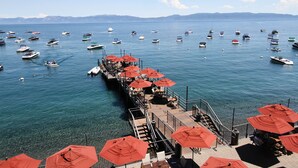 Une jetée agrémentée de parasols rouges et de tables, d’où l’on a vue sur un port de plaisance où sont amarrés de nombreux bateaux.