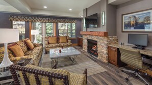 A spacious living room with a stone fireplace, comfortable seating, a flat-screen TV, and a large window with a view of trees. - WorldMark McCall (McCall)